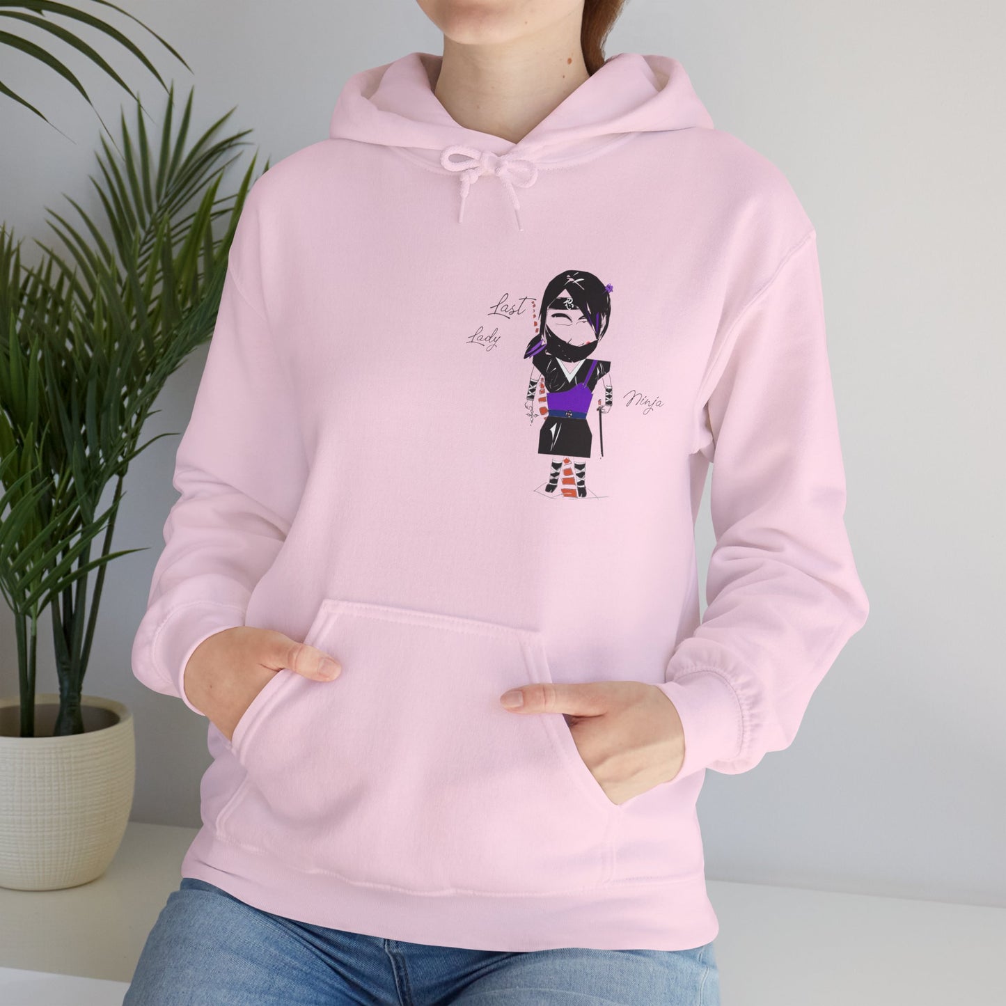 A lady model wearing a pink hoodie with a lady ninja graphic design on a neutral background