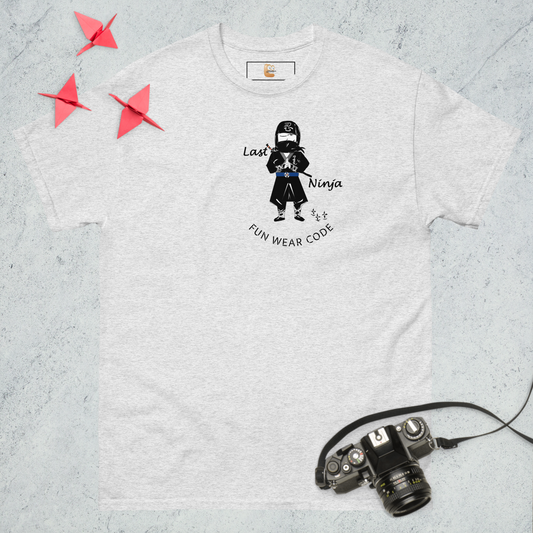 Ash gray t-shirt with a playful ninja graphic design and text "FUN WEAR CODE", placed on a textured surface with a camera and origami birds.