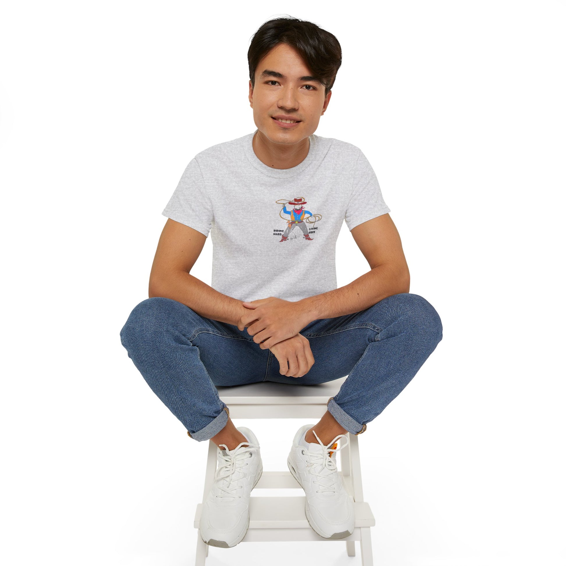 Front view of a man model wearing a gray t-shirt with a cowboy graphic design, sitting on a white stool against a white background