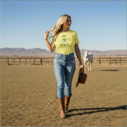 Woman in a yellow t-shirt with a playful cowgirl graphic design and text, and blue jeans walking in a field with a horse in the background