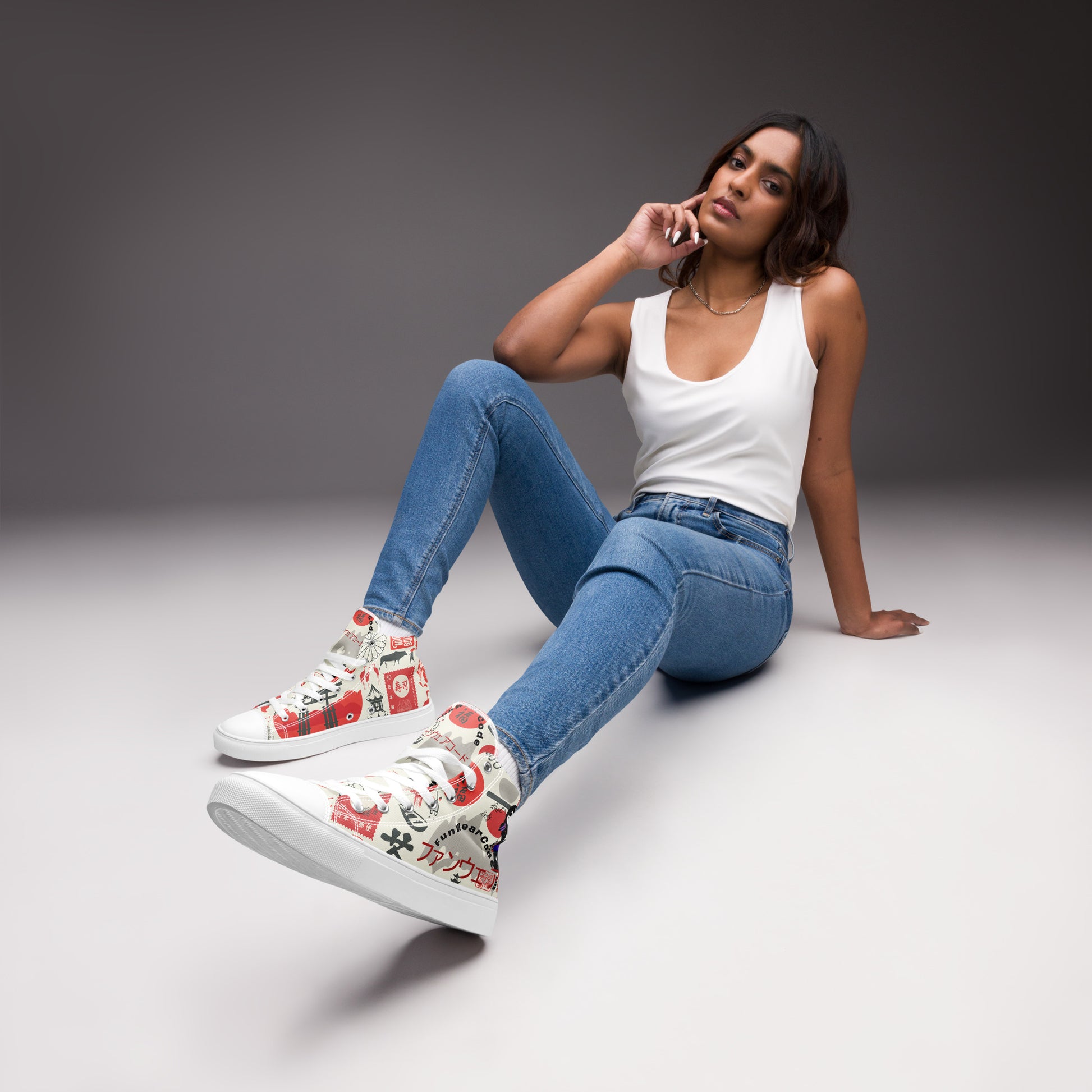 Woman sitting on a gray floor wearing a pair of high-top sneakers with colorful Japanese elements graphic design, and with a ninja graphic and 'Fun Wear Code' text logo, blue jeans, and a white tank top.